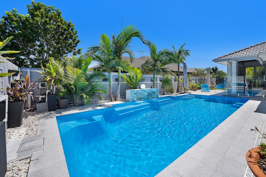 Fibreglass pool surrounded by tropical palms and garden beds
